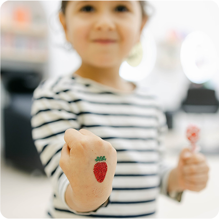 Child with a temporary tattoo of a red heart on their wrist, holding a lollipop.