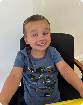 Child wearing a blue t-shirt with vehicle prints, sitting on a chair indoors.
