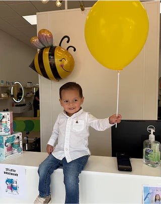 Child holding a yellow balloon with a bee-shaped object in the background