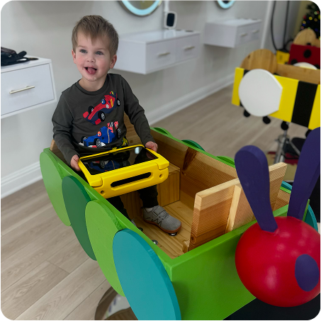Child playing with a colorful toy car shaped like a caterpillar in a room.