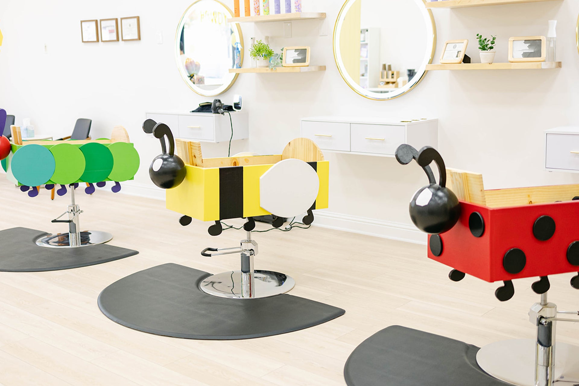 Children's salon chairs designed like ladybugs in a bright room with mirrors and shelves.