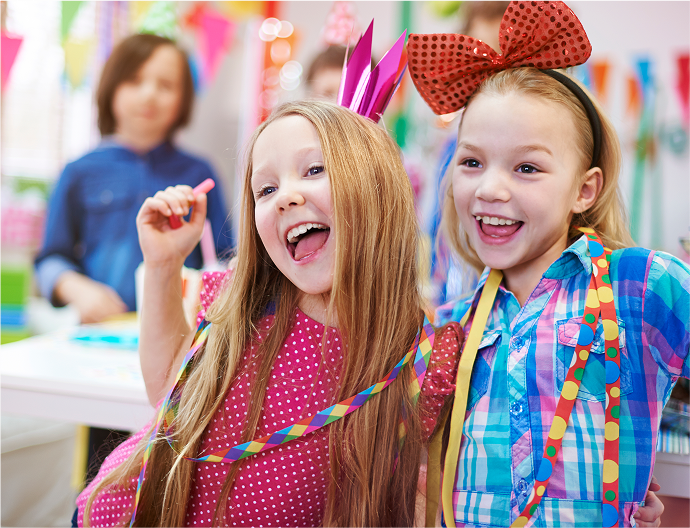 Two young girls with festive headbands and ribbons in a classroom setting.