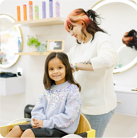 Woman with colorful hair styling a young girl in a salon setting.