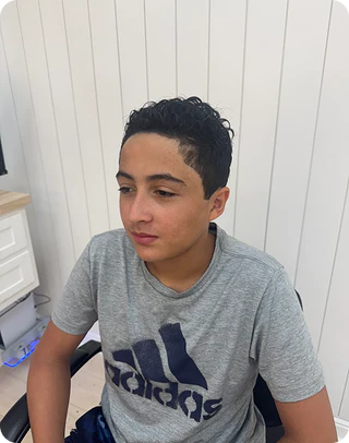 Boy wearing a gray Adidas t-shirt sitting in front of a white wall.