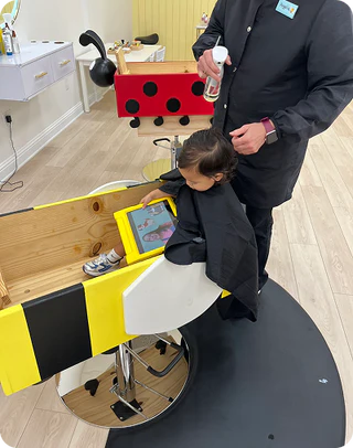 Child sitting in a salon chair with a hairdresser preparing to cut their hair.